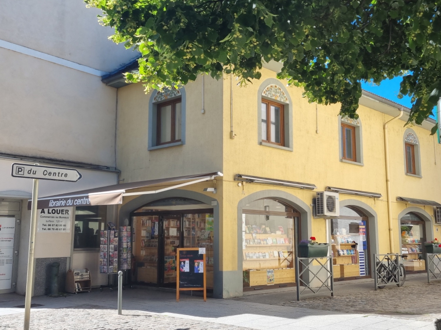 La devanture jaune de la Librairie du Centre, avec son store « librairie du centre » et ses vitrines en arcade, dans le Ferney ancien