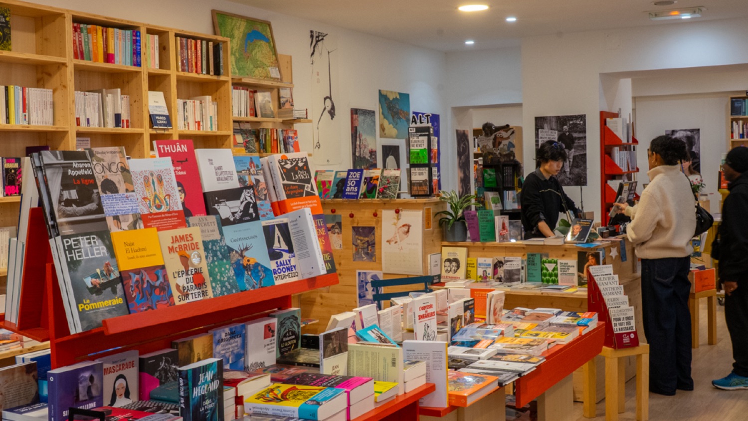 Intérieur de la librairie : rayonnages en bois, tables de nouveautés colorées et un libraire au comptoir